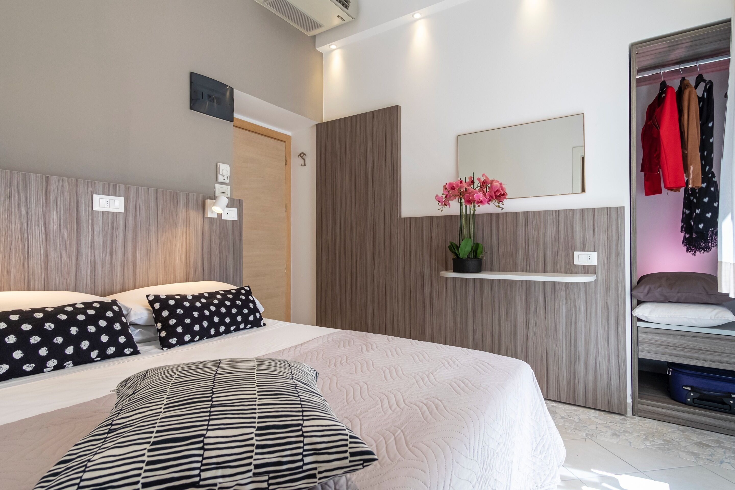 A modern bedroom with a large bed, a bedside table, a mirror, and a wardrobe.