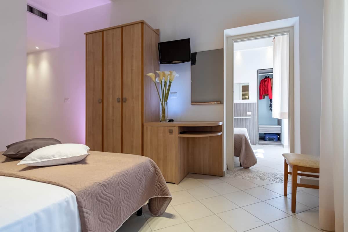 Une chambre d’hôtel comprenant un lit, une armoire en bois, un bureau, un miroir et un téléviseur.