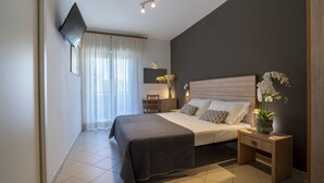 A modern bedroom with a large bed, bedside tables, a flat-screen TV, and a vase with flowers. - Hotel Mocambo (Riccione)