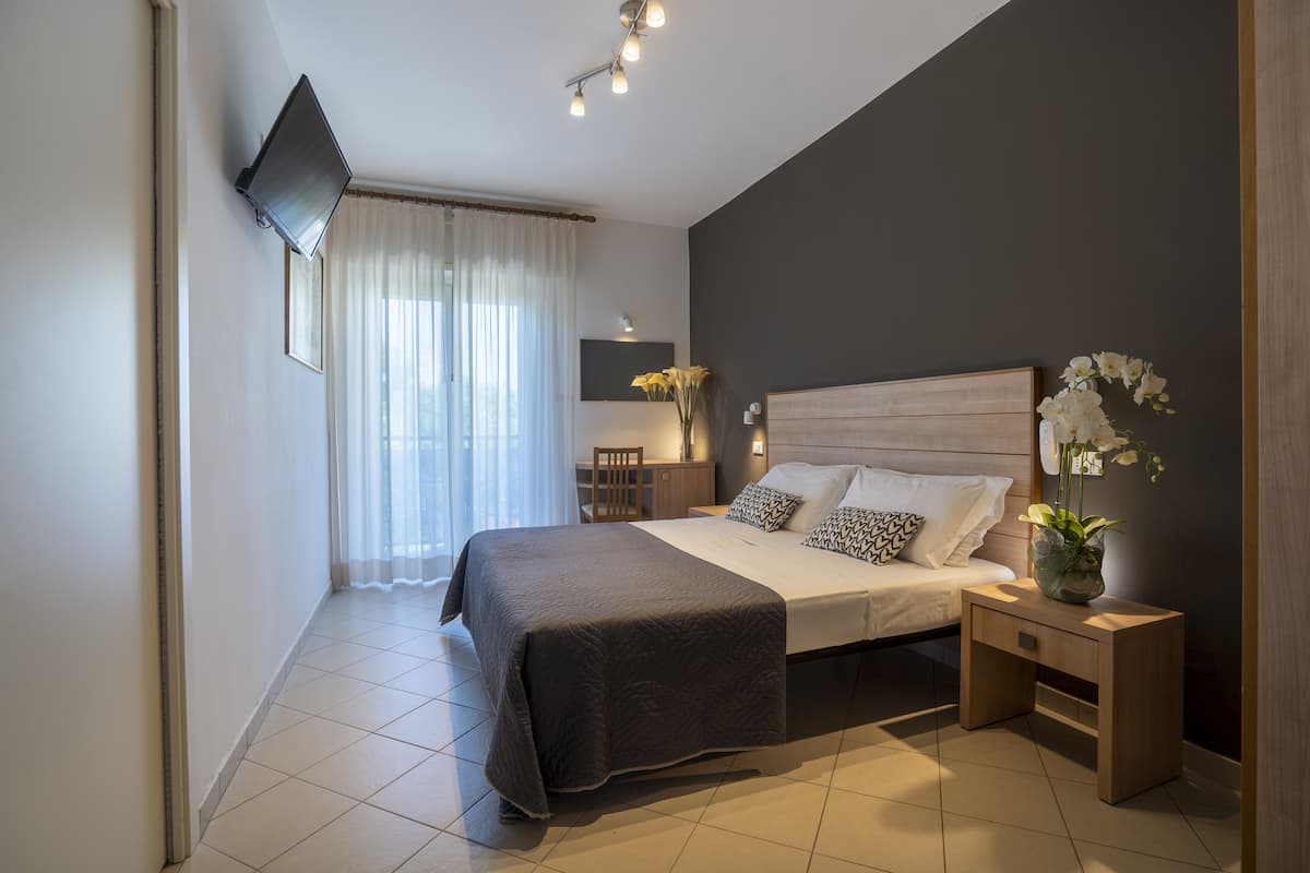 Une chambre à coucher moderne avec un grand lit, des tables de chevet, un téléviseur à écran plat et un vase rempli de fleurs.