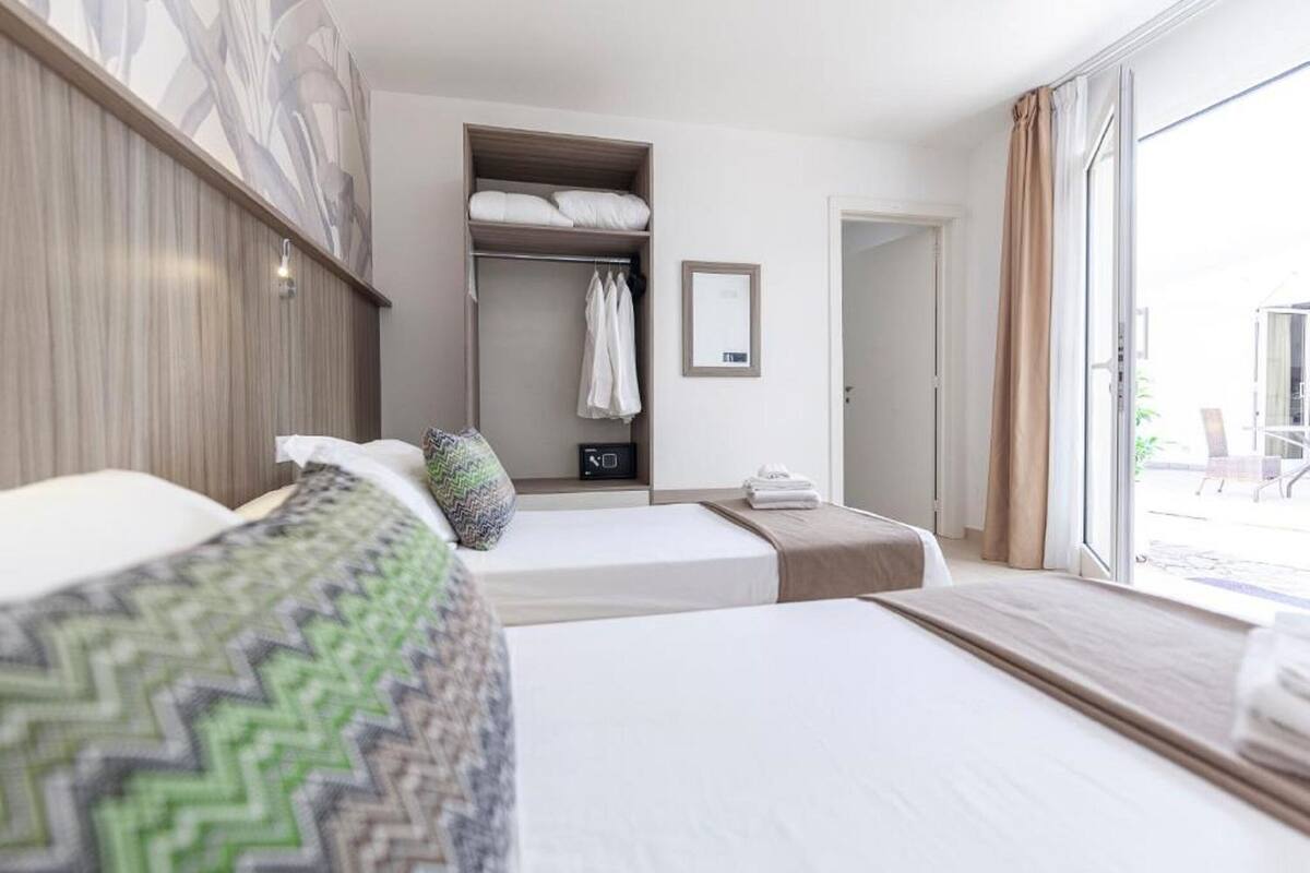 Ein Hotelzimmer mit zwei Betten, einem Schrank, einem Spiegel und einer Schiebetür zum Außenbereich.