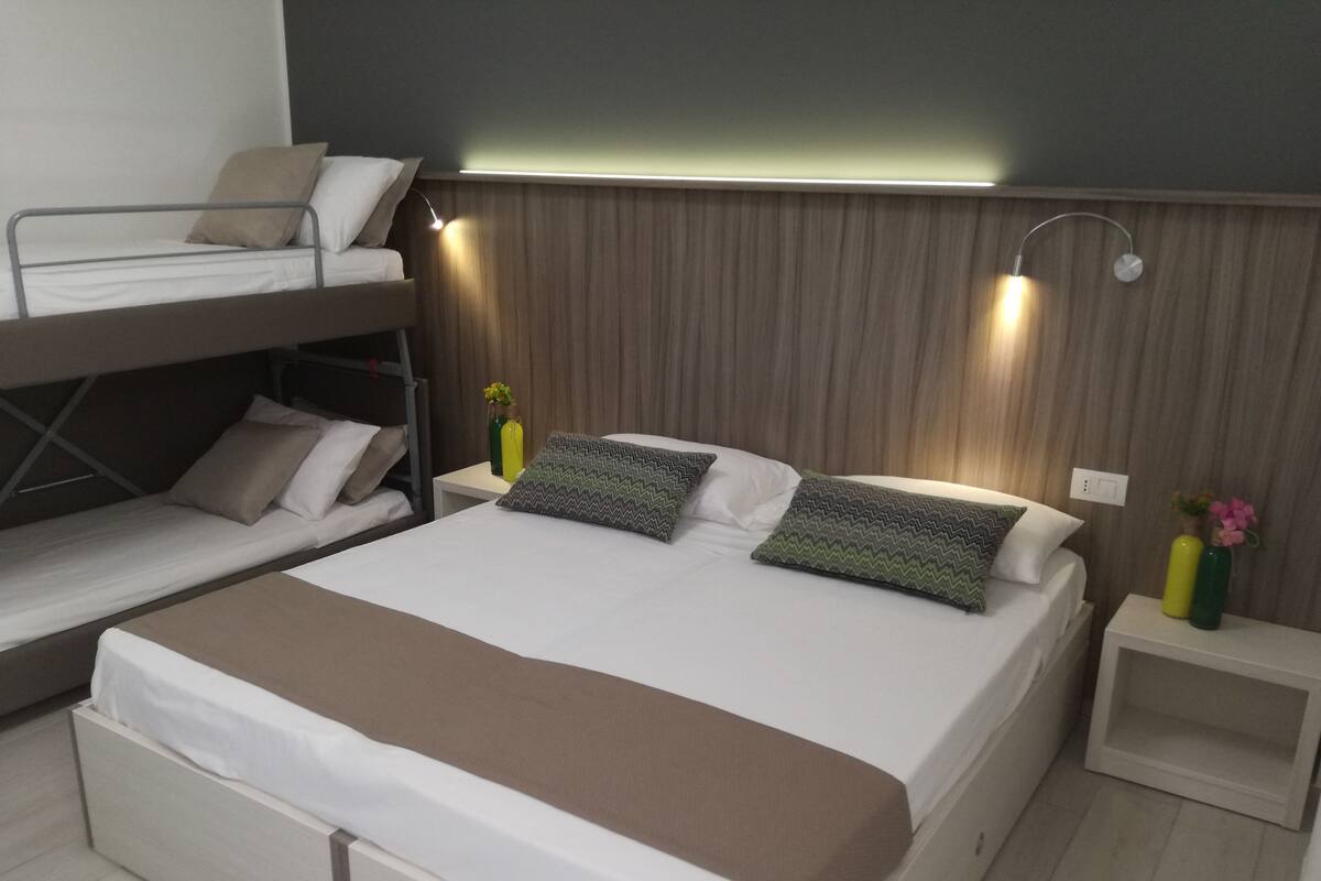 Ein Hotelzimmer mit einem Etagenbett, einem Einzelbett und einem Nachttisch mit Lampe.
