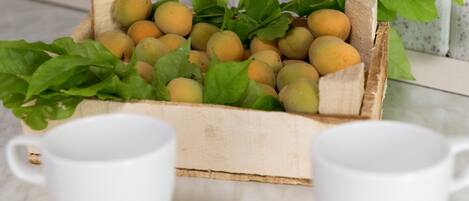 Una caja de madera llena de frutas amarillas y hojas verdes, sobre una superficie de mármol con tazas blancas al frente.