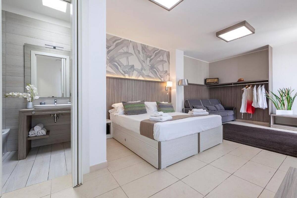 Ein modernes Hotelzimmer mit einem großen Bett, einem Schminktisch mit Spiegel, einer kleinen Sitzecke und einem Kleiderschrank.