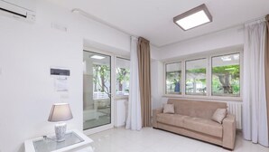 Ein modernes Wohnzimmer mit einem beigefarbenen Sofa, einem Glastisch und einem großen Fenster mit Vorhängen.
