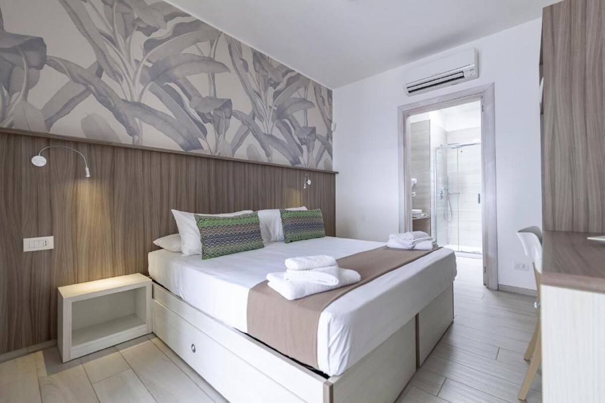 Une chambre d’hôtel moderne équipée d’un grand lit, d’une table de chevet, d’une armoire et d’un espace douche.