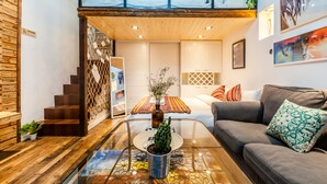 Un interior moderno con un entrepiso con dormitorio, una mesa de centro de cristal y un sofá gris.