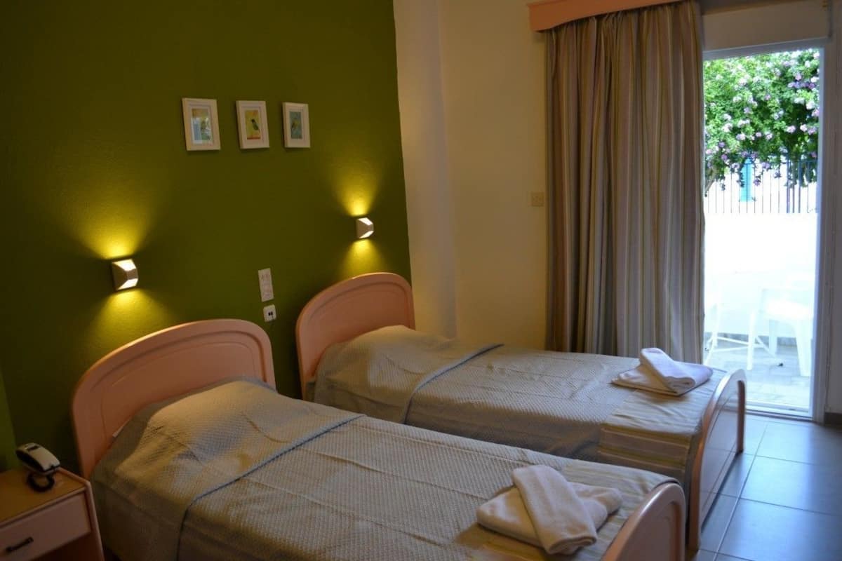 Quarto de hotel com duas camas, uma parede verde e uma janela com cortinas.