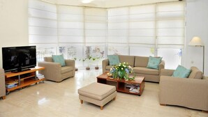 A spacious living room with a large flat-screen TV, two sofas, a coffee table, and a TV stand. - Ifigenia Hotel (Skiathos)