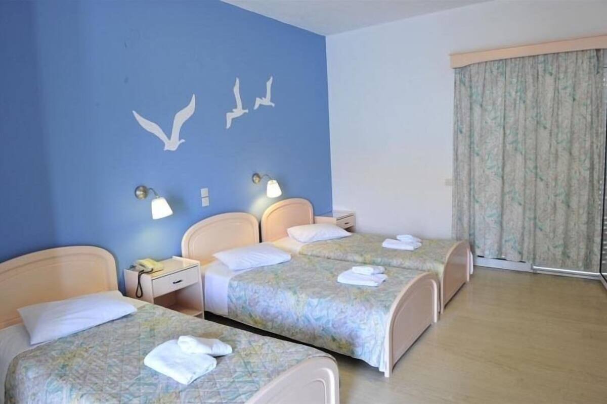 Quarto de hotel com duas camas, parede azul com silhuetas de pássaros, janela com cortinas e abajures nas mesas de cabeceira.