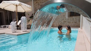 Une piscine agrémentée d’un élément décoratif aquatique, de chaises longues et d’un mur en pierre.