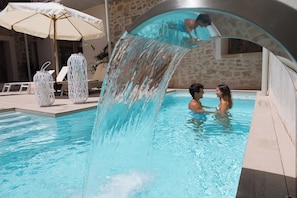 A swimming pool with a water feature, lounge chairs, and a stone wall. - Forum Boutique Hotel & Spa (Alcúdia)