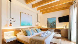 Une chambre d’hôtel moderne avec un plafond en bois, un lit recouvert d’une couverture beige, un bureau avec une chaise et des œuvres d’art accrochées aux murs.