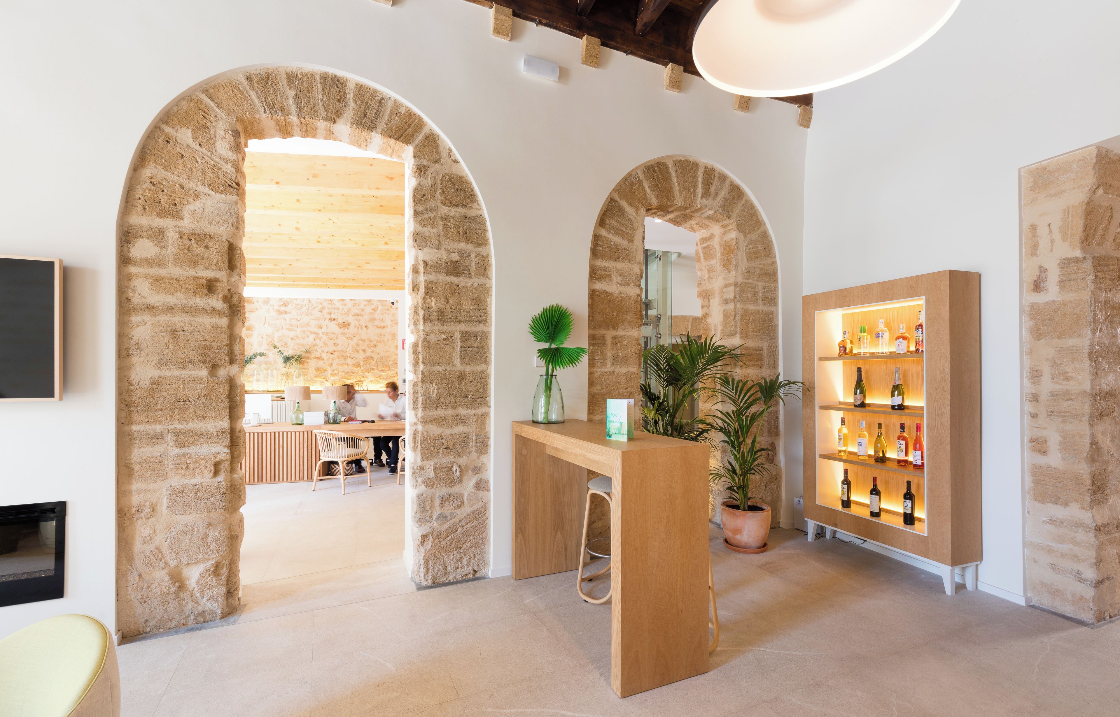 Un interior moderno con arcos de piedra, una recepción de madera y una vitrina de vinos.