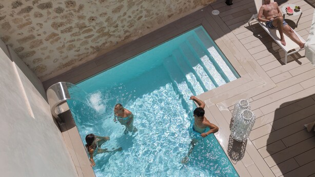 Une piscine à l’eau claire, entourée d’une terrasse carrelée et de murs en pierre.