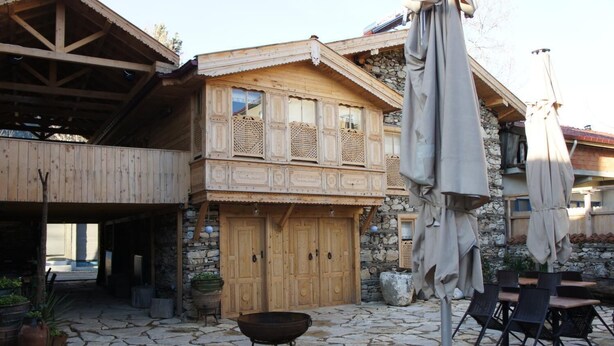 A rustic wooden building with a stone-paved courtyard, a large wooden door, and outdoor seating with umbrellas.