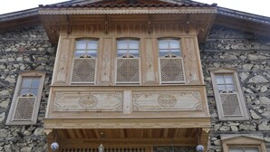 A wooden building with a stone facade, featuring a balcony with decorative lattice windows and a stone wall.