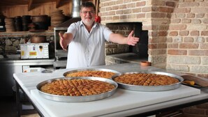 A chef presenting baked goods in a kitchen with a brick oven and various cooking utensils.