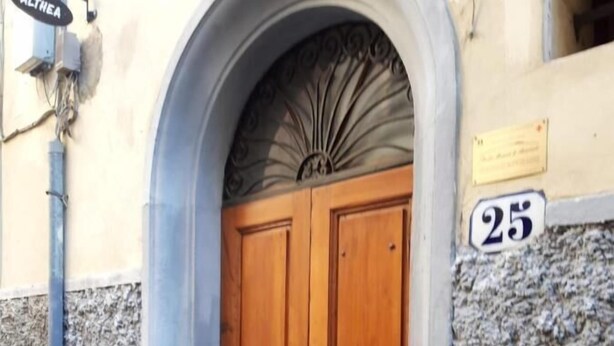 Une porte à deux battants en bois, adossée à un mur de pierre, et une enseigne portant le nom « ALTHEA » au-dessus.