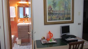 Une pièce comprenant un bureau, un ordinateur, un tableau et une salle de bain visible à travers une porte ouverte.