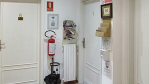 Un couloir avec des portes blanches, un extincteur, un radiateur et une poubelle.