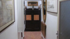 Un couloir étroit avec un banc, un réfrigérateur, un buffet en bois sombre et un miroir accroché au mur.