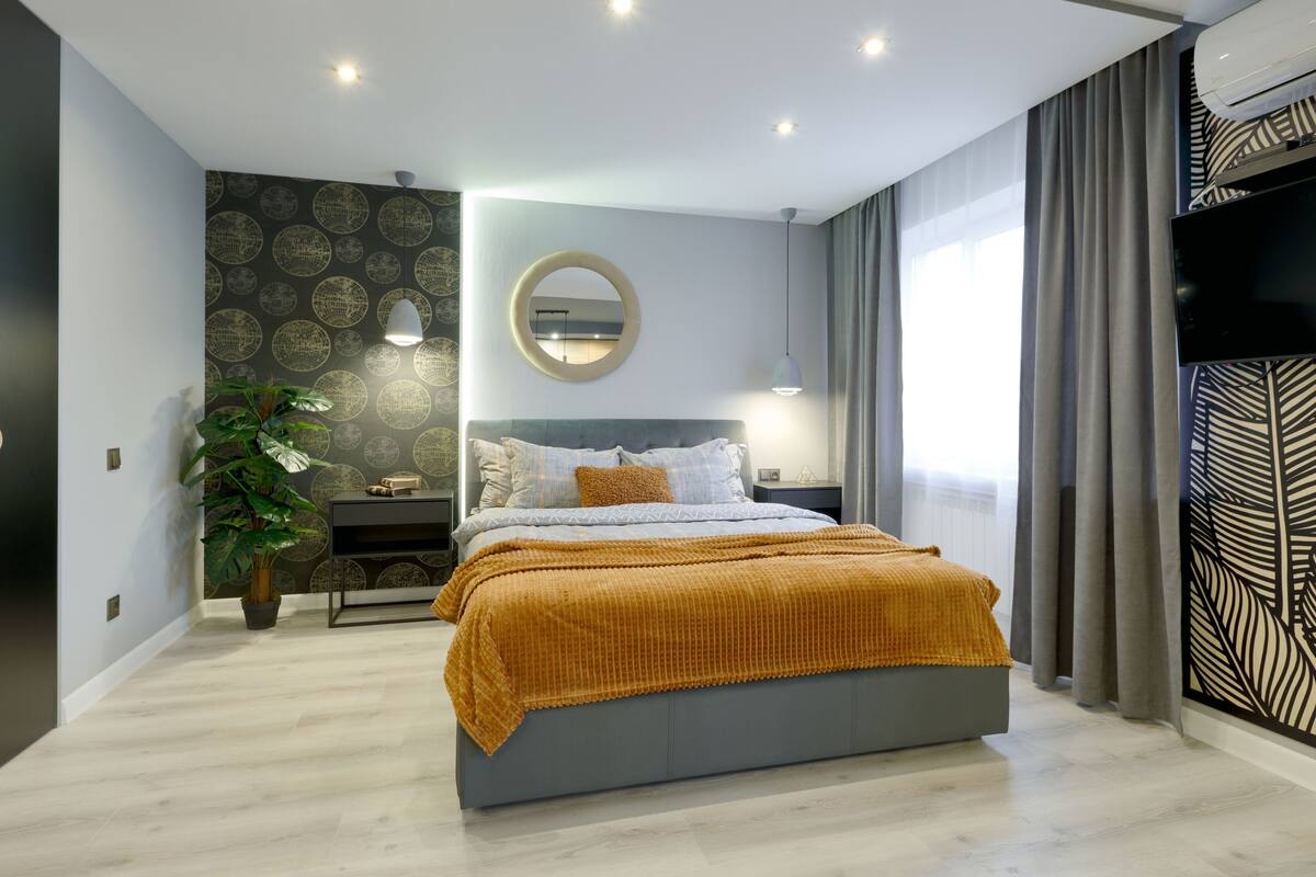 A modern bedroom with a bed, a bedside table, a mirror, a potted plant, and a TV.