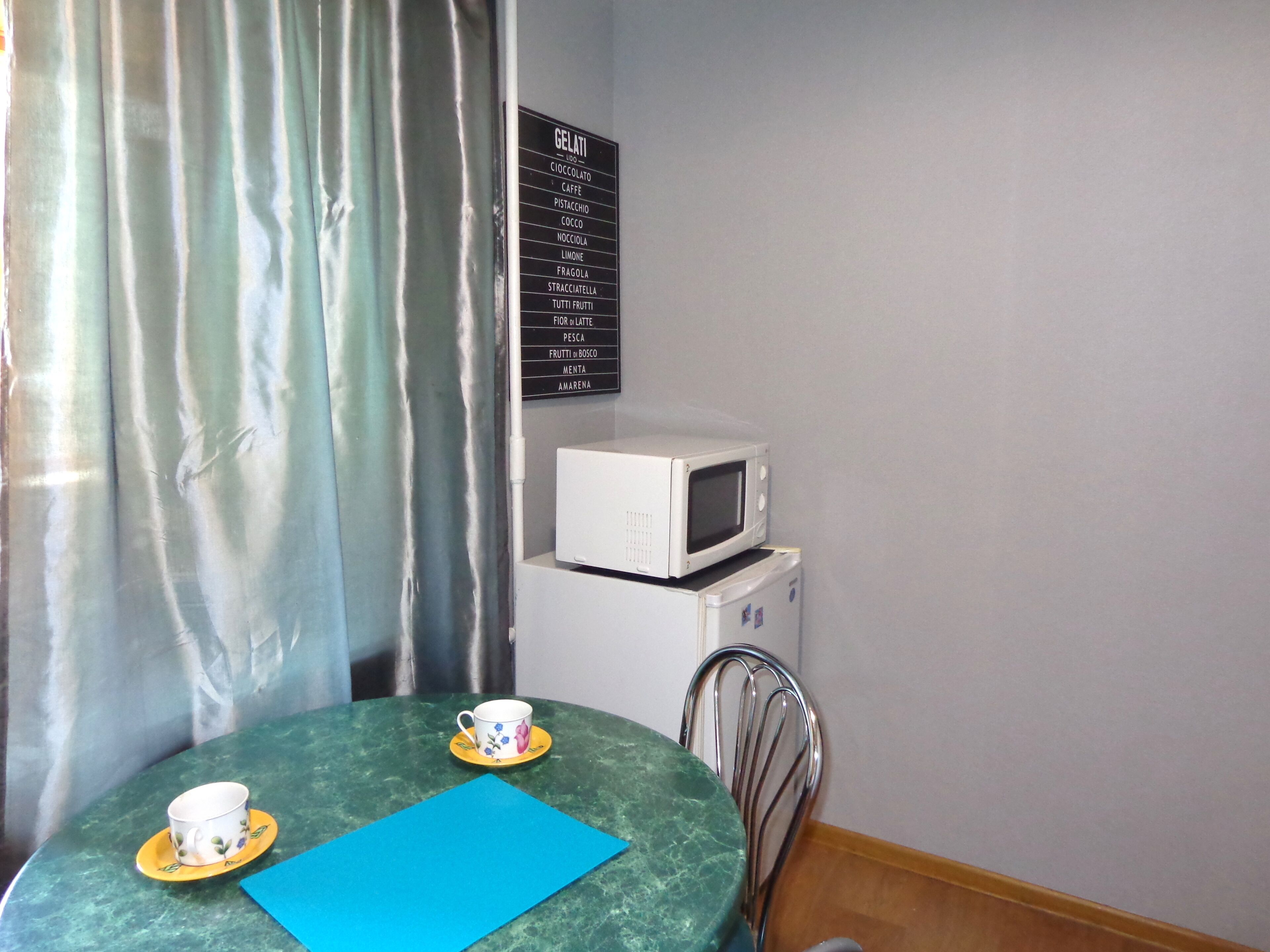 Un pequeño comedor con una mesa, dos tazas, un mantel azul, un microondas blanco y un panel con los sabores de helados.