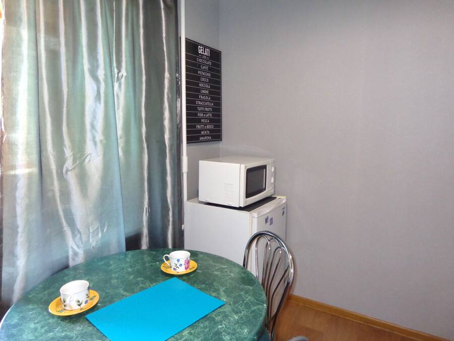 Un pequeño comedor con una mesa, dos tazas, un mantel azul, un microondas blanco y un panel con los sabores de helados.