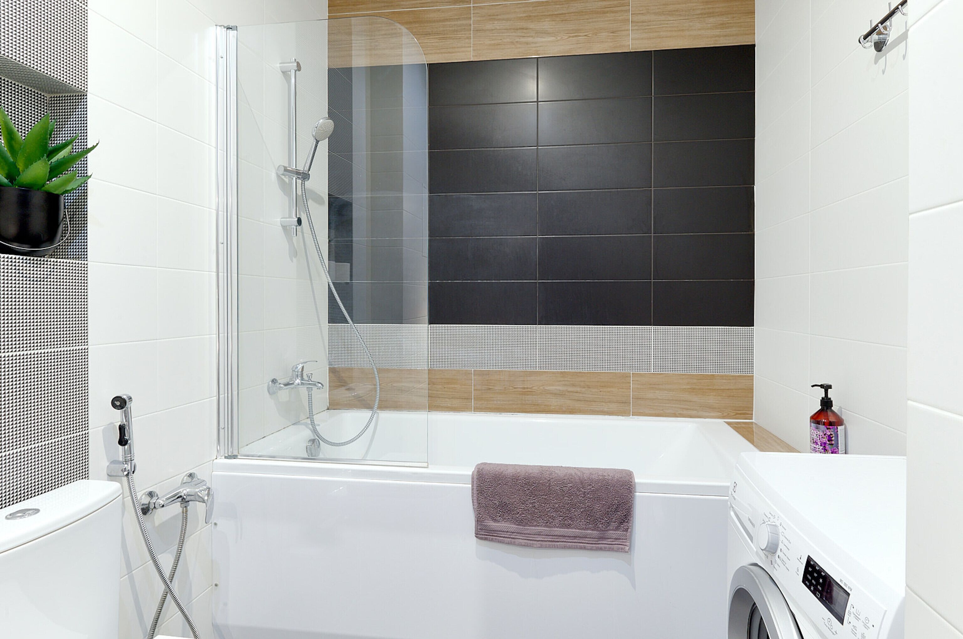 Une salle de bain moderne avec une douche à parois de verre, une baignoire blanche et un lave-linge encastré.