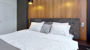 Une chambre moderne avec un grand lit, une tête de lit en bois et deux lampes suspendues.