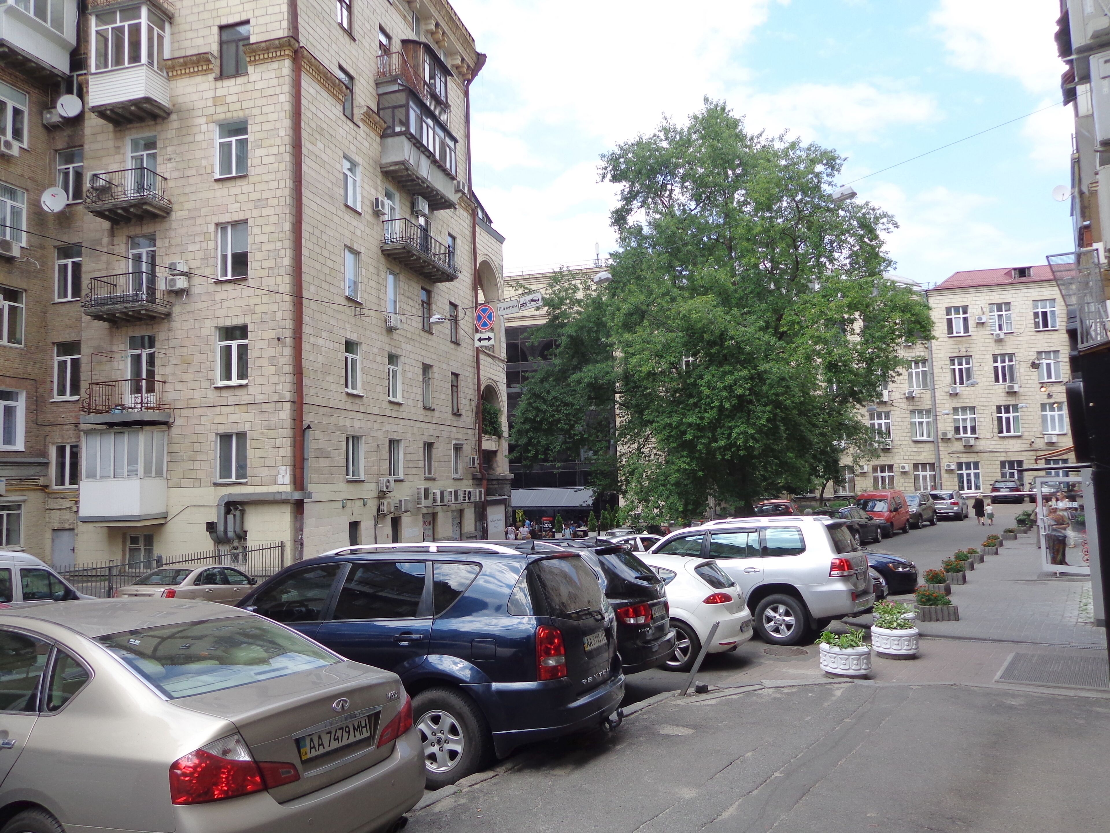 A multi-story building with balconies, parked cars, and a pedestrian walkway.