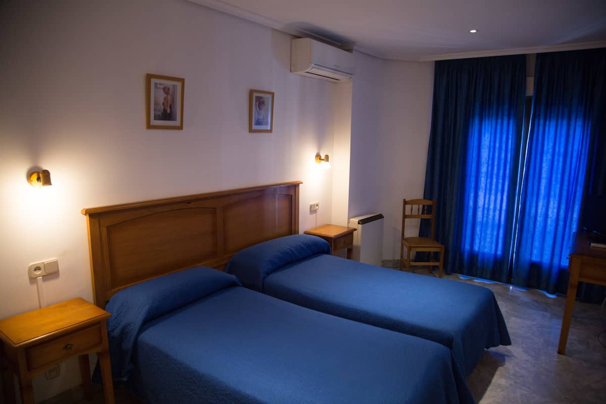 Habitación de hotel con dos camas, cabeceros de madera, mesitas de noche, un escritorio y una silla.