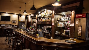 A bar area with wooden bar counters, multiple stools, and a variety of liquor bottles. - Hostal Acuario (Galvez)