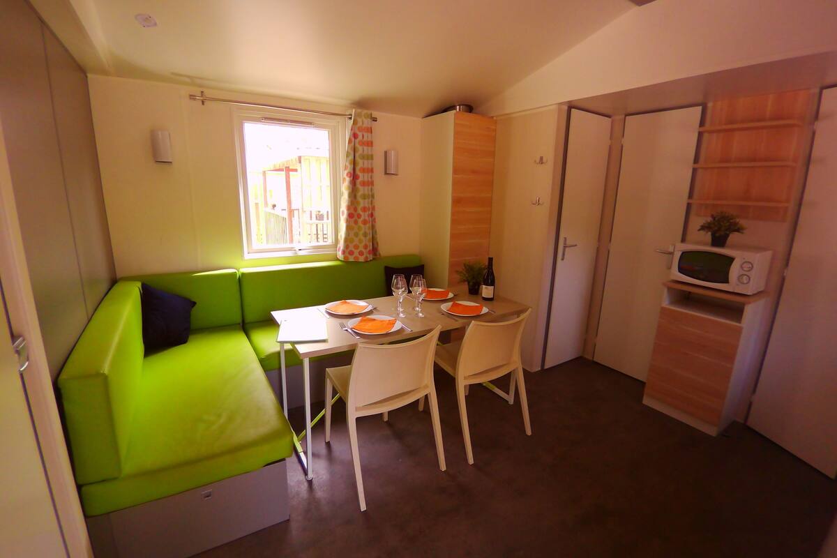 A compact kitchen with a dining table, chairs, a microwave, and a window with curtains.