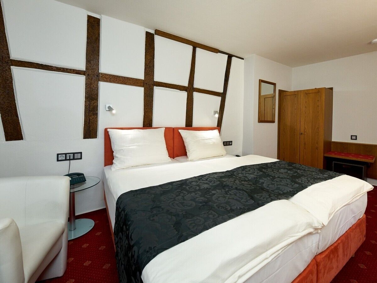 A hotel room with a large bed, a bedside table, a chair, a wardrobe, and a mirror on the wall.