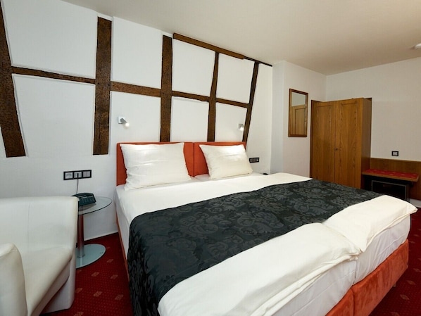 A hotel room with a large bed, a bedside table, a chair, a wardrobe, and a mirror on the wall. - Hotel zur Post (Bernkastel-Kues)