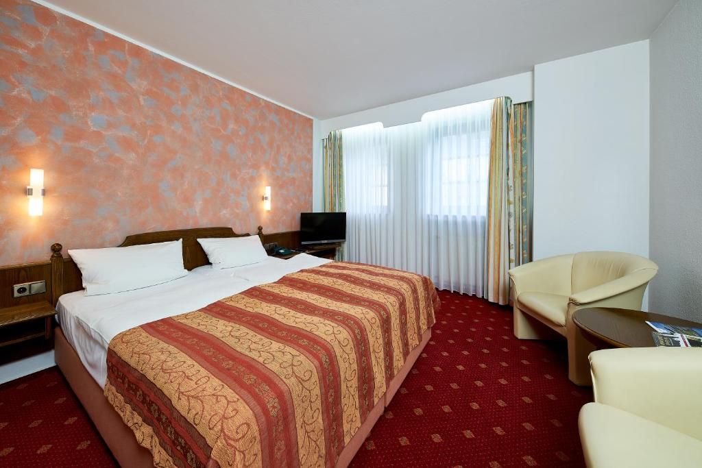 A hotel room with a large bed, a TV, a chair, and a desk.