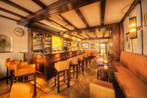 Zona de bar con vigas de madera, taburetes y barra con botellas y vasos.