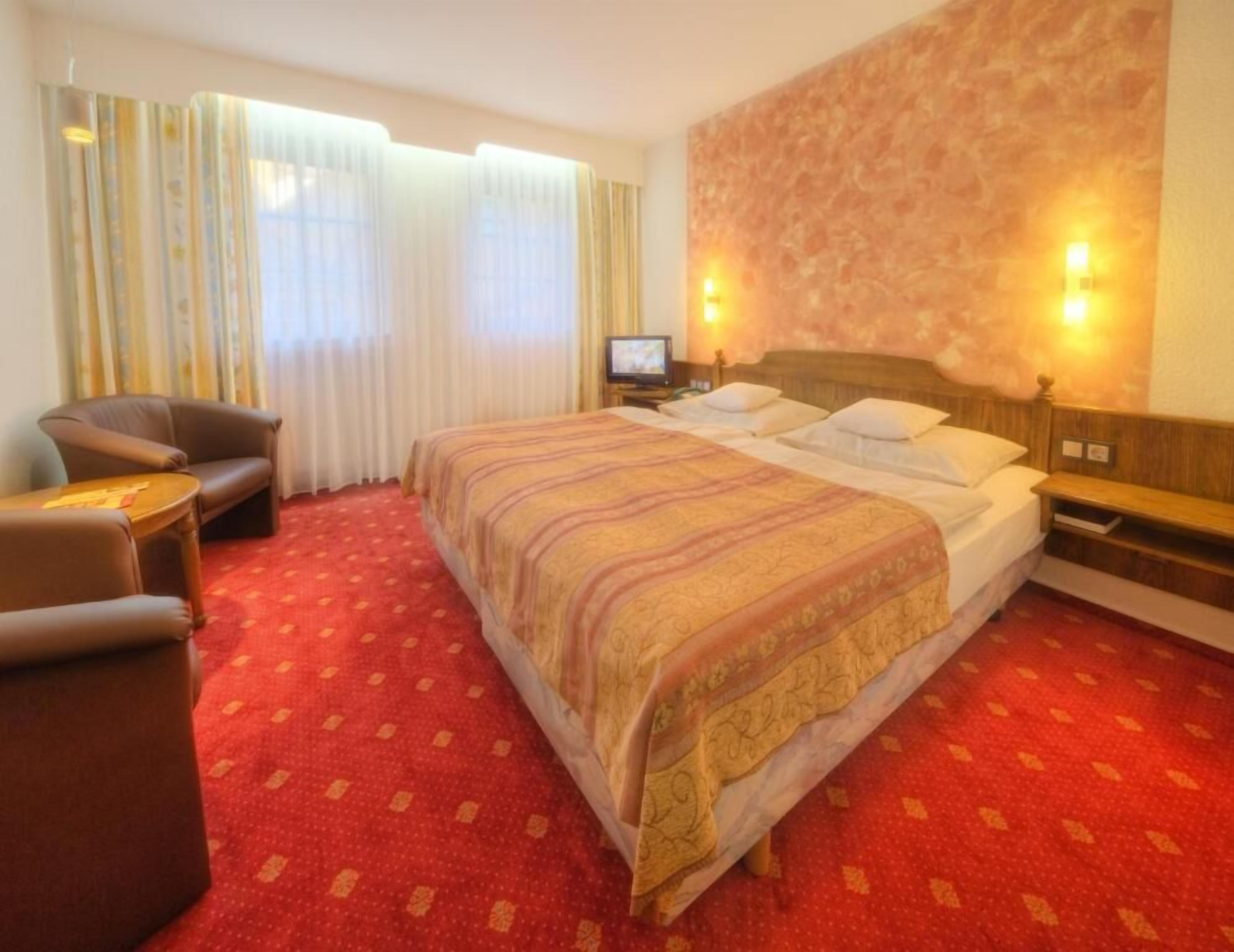 A hotel room with a large bed, a desk, a chair, and a television.