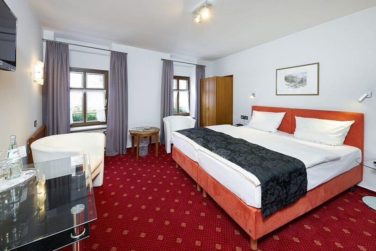 A hotel room with a bed, a desk, a chair, a small table, and a window with curtains.