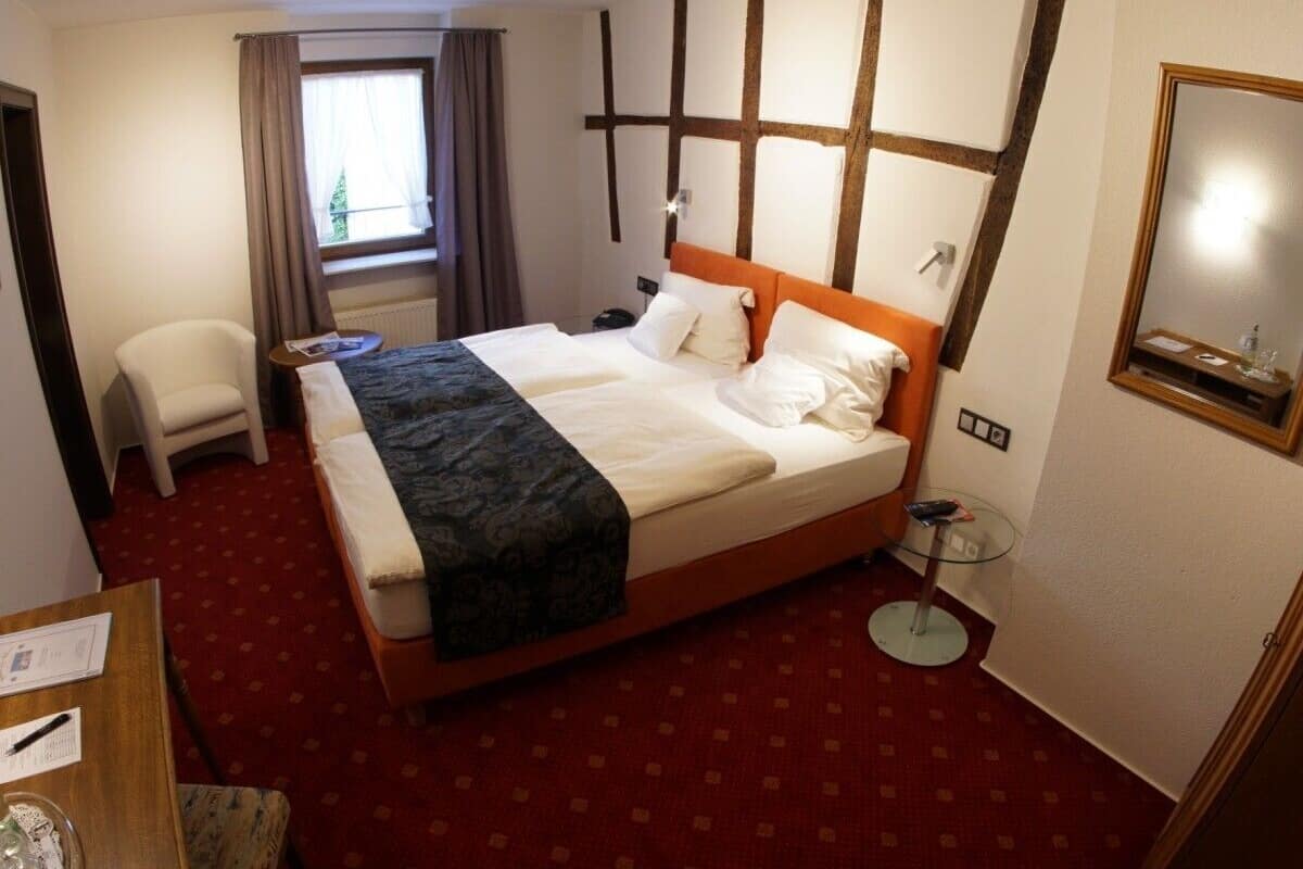 A hotel room with a large bed, a chair, a small table, and a window with curtains.