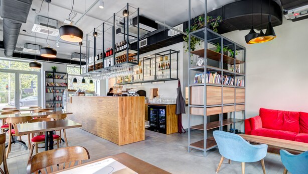 A modern cafe with wooden tables and chairs, a red sofa, and shelves with books and bottles. - Ratusz B&B (Gdansk)