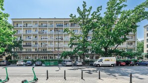 Un immeuble résidentiel à plusieurs étages, doté de balcons, avec des voitures garées et un scooter vert sur le trottoir.