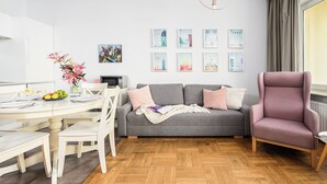 Un salon moderne avec un canapé gris, un fauteuil rose et une table à manger agrémentée de chaises blanches.