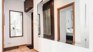 Un couloir avec une porte en bois, un miroir et un lit visible à travers une pièce adjacente.