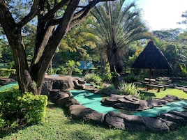 Un jardín tropical con un estanque, rocas y una estructura con techo de paja.