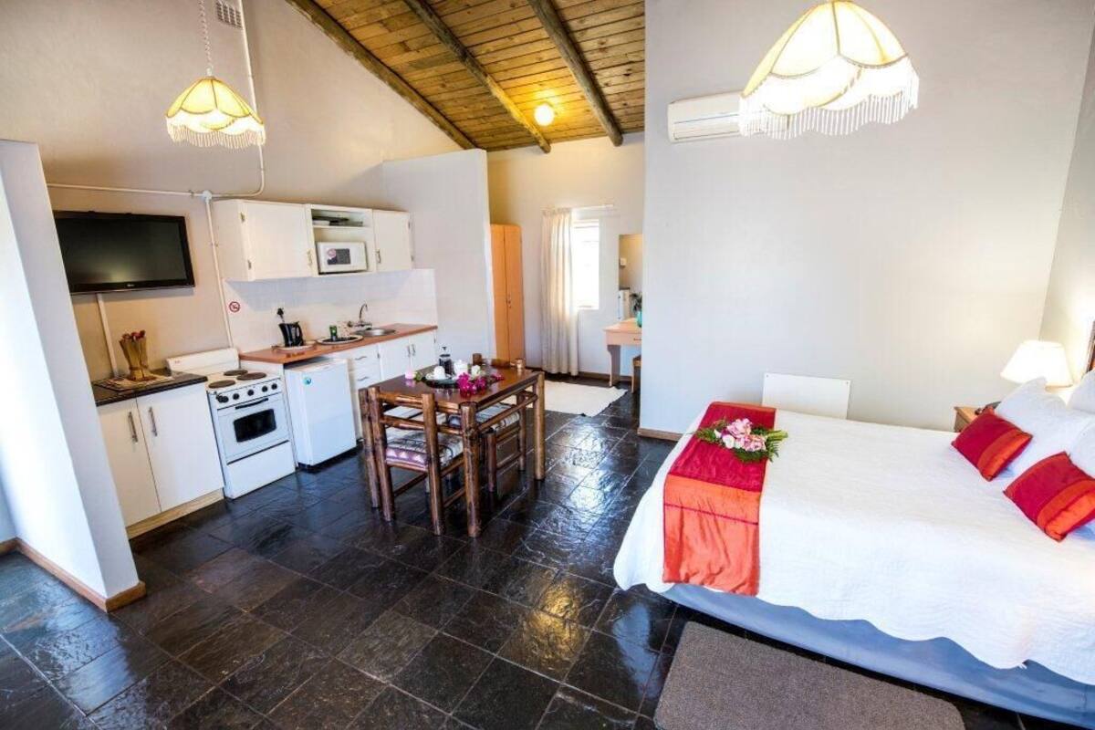 Una habitación de hotel compacta con kitchenette, zona de comedor y cama con cabecero decorativo.