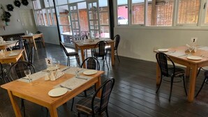 A dining area with wooden tables and chairs, numbered placemats, and a view through large windows. - Brookside Lodge B&B (Matsapha)