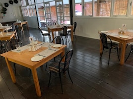 Un comedor con mesas y sillas de madera, manteles individuales numerados y vistas amplias a través de grandes ventanales.